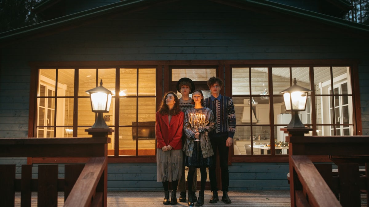 Group celebrating Hanukkah on porch, holding lit menorah, cozy winter evening.